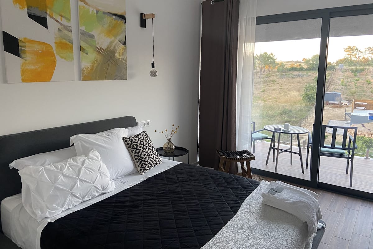 A bedroom with a large bed, a view of the outdoors through a sliding glass door, and abstract art on the wall.