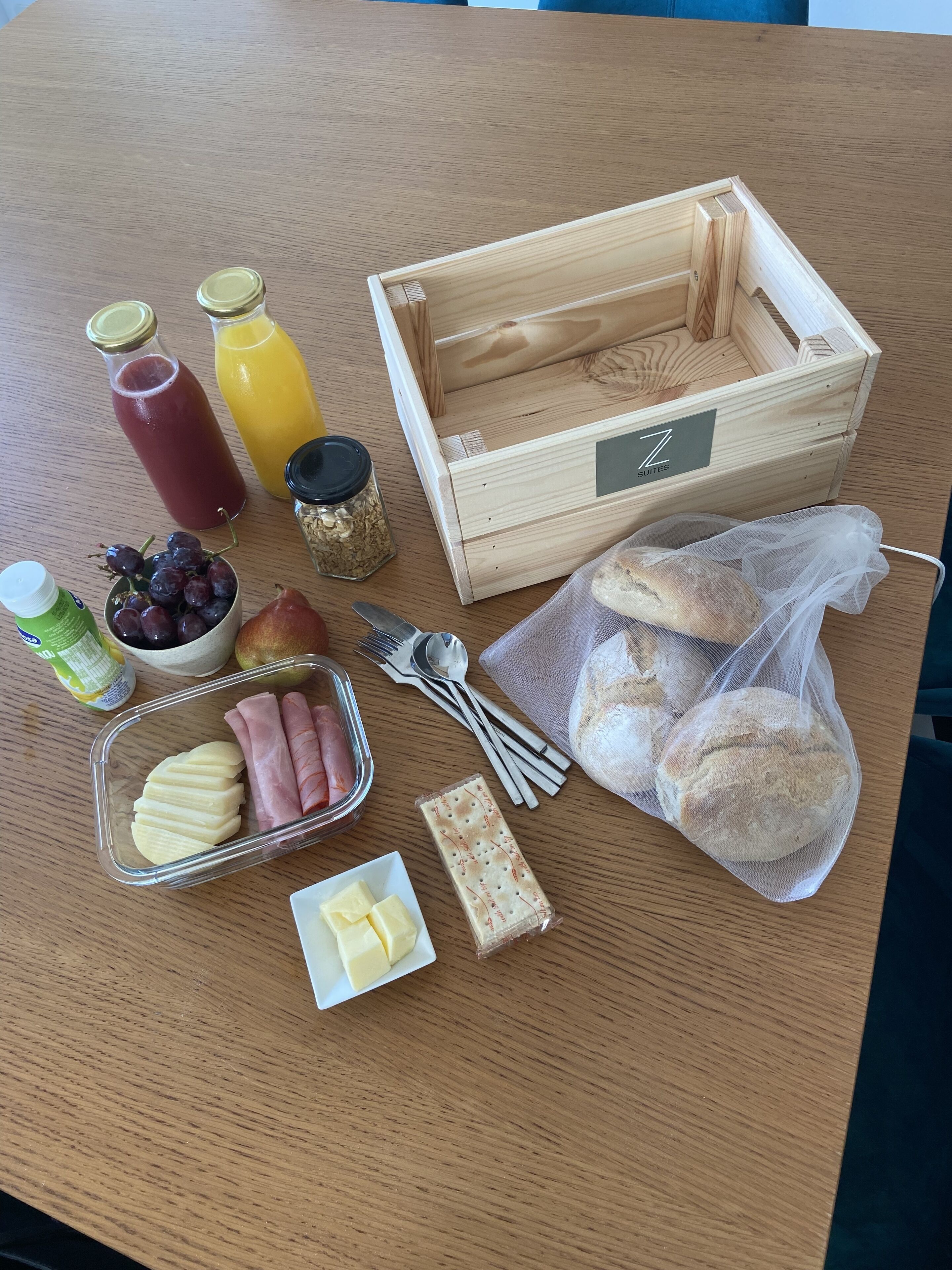 A wooden table with a variety of food items including fruits, bread, cheese, and condiments.