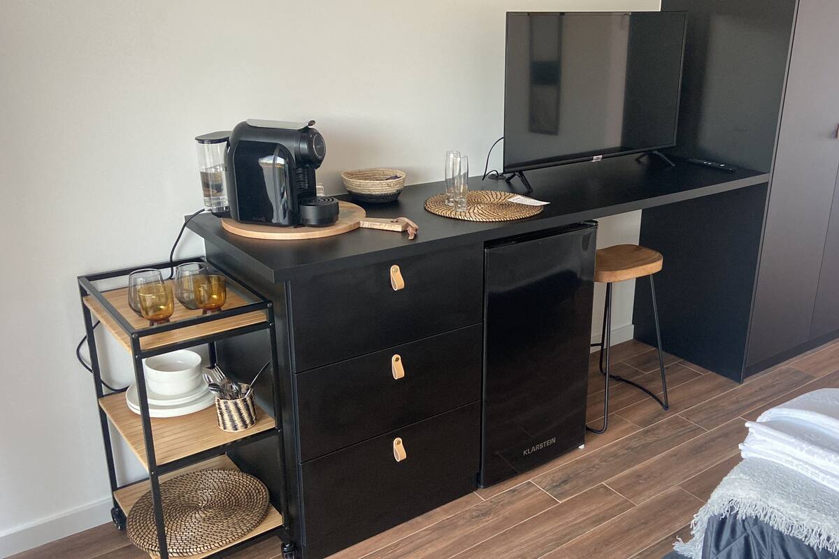 A compact kitchenette with a black refrigerator, a coffee maker, and a small bar area.