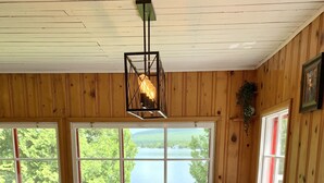 Un coin repas avec une table et des chaises en bois, de grandes fenêtres donnant sur un lac et un luminaire suspendu.
