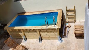Ein Holzschwimmbecken mit Metallleitern, umgeben von Baumaterialien und Werkzeugen.
