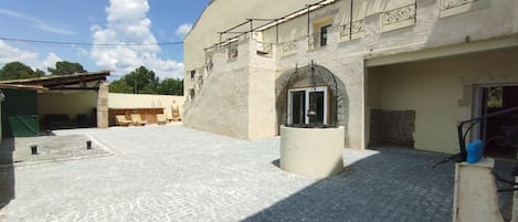 A courtyard with a stone floor, a fountain, and a building with an arched entrance.