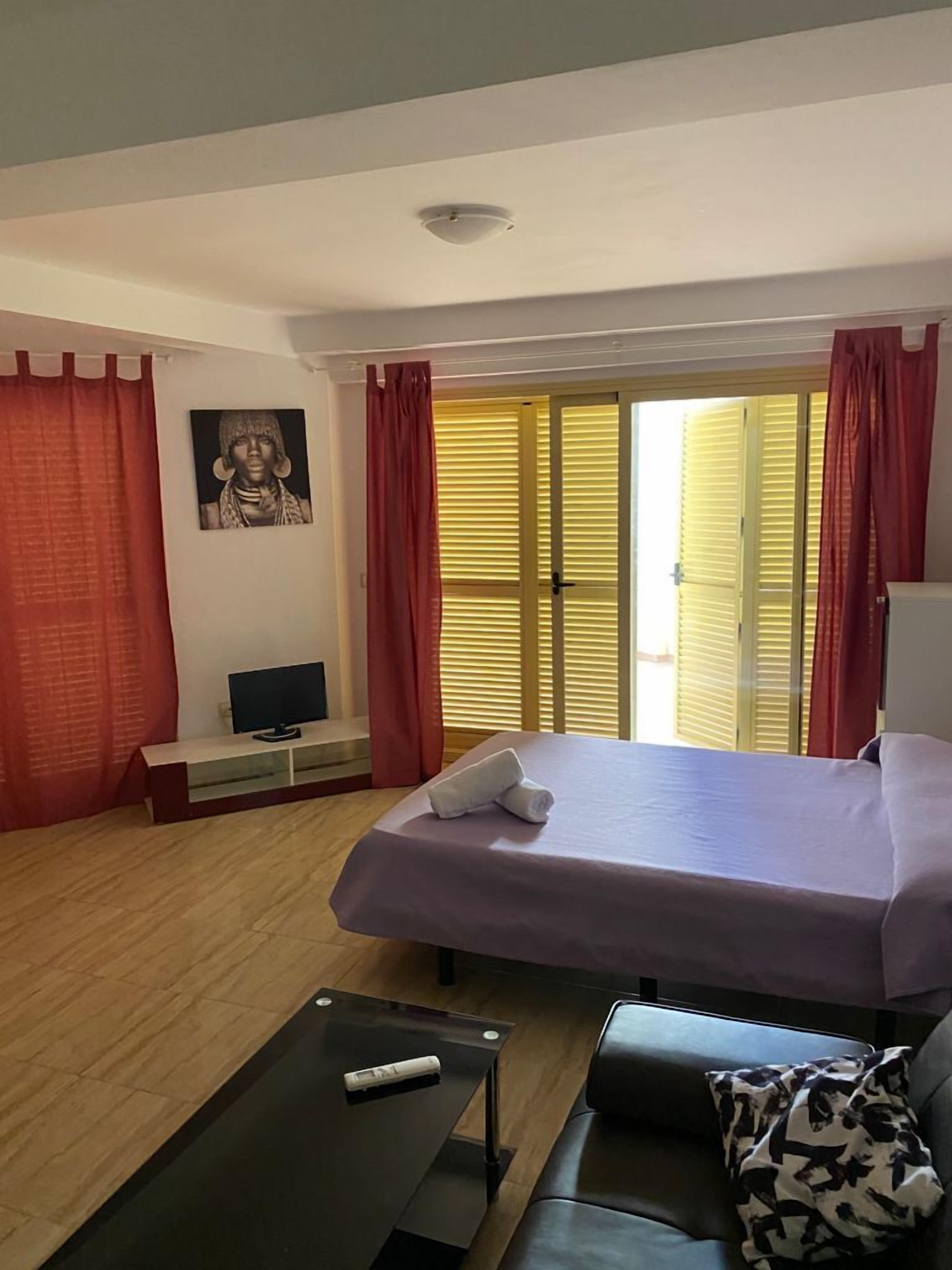 A hotel room with a bed, a TV, a coffee table, a sofa, and a window with curtains.