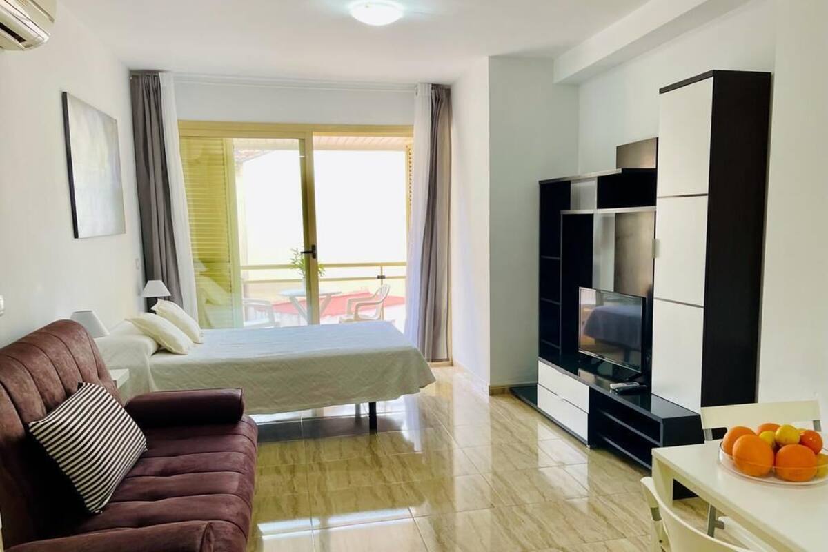 Una habitación de hotel moderna con cama, sofá, televisor y zona de comedor.
