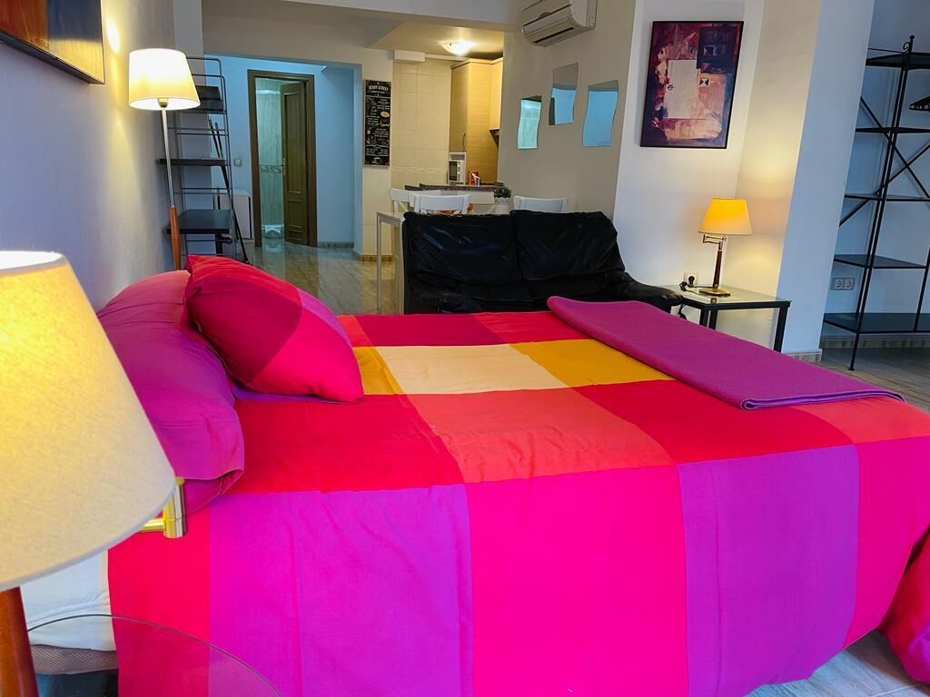 Un letto con una coperta colorata, una lampada da comodino e un tavolino con una lampada.