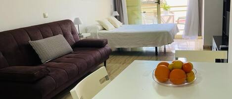 Una sala de estar con un sofá, una mesa de comedor con fruta, una cama y un balcón con vistas.