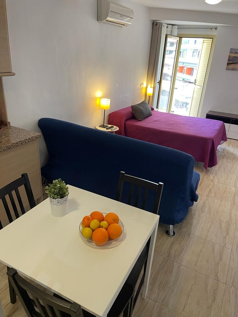 A compact living space with a dining table, a blue sofa, a red sofa, and a small kitchen area.
