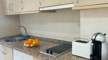 Une cuisine équipée d’un lave-linge, d’un grille-pain et d’un panier à fruits posé sur le plan de travail.
