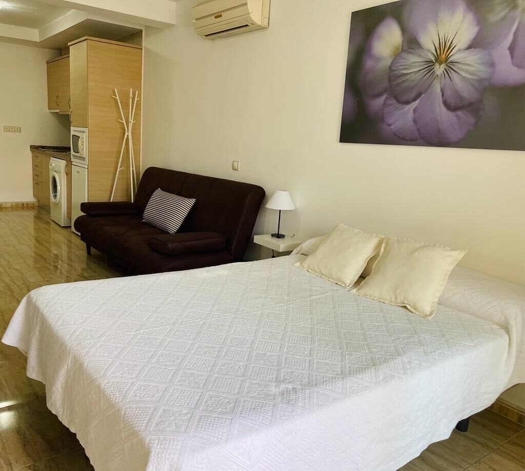 Habitación de hotel con cama, una silla, mesita de noche, lámpara, equipo de aire acondicionado y un cuadro colgado en la pared.