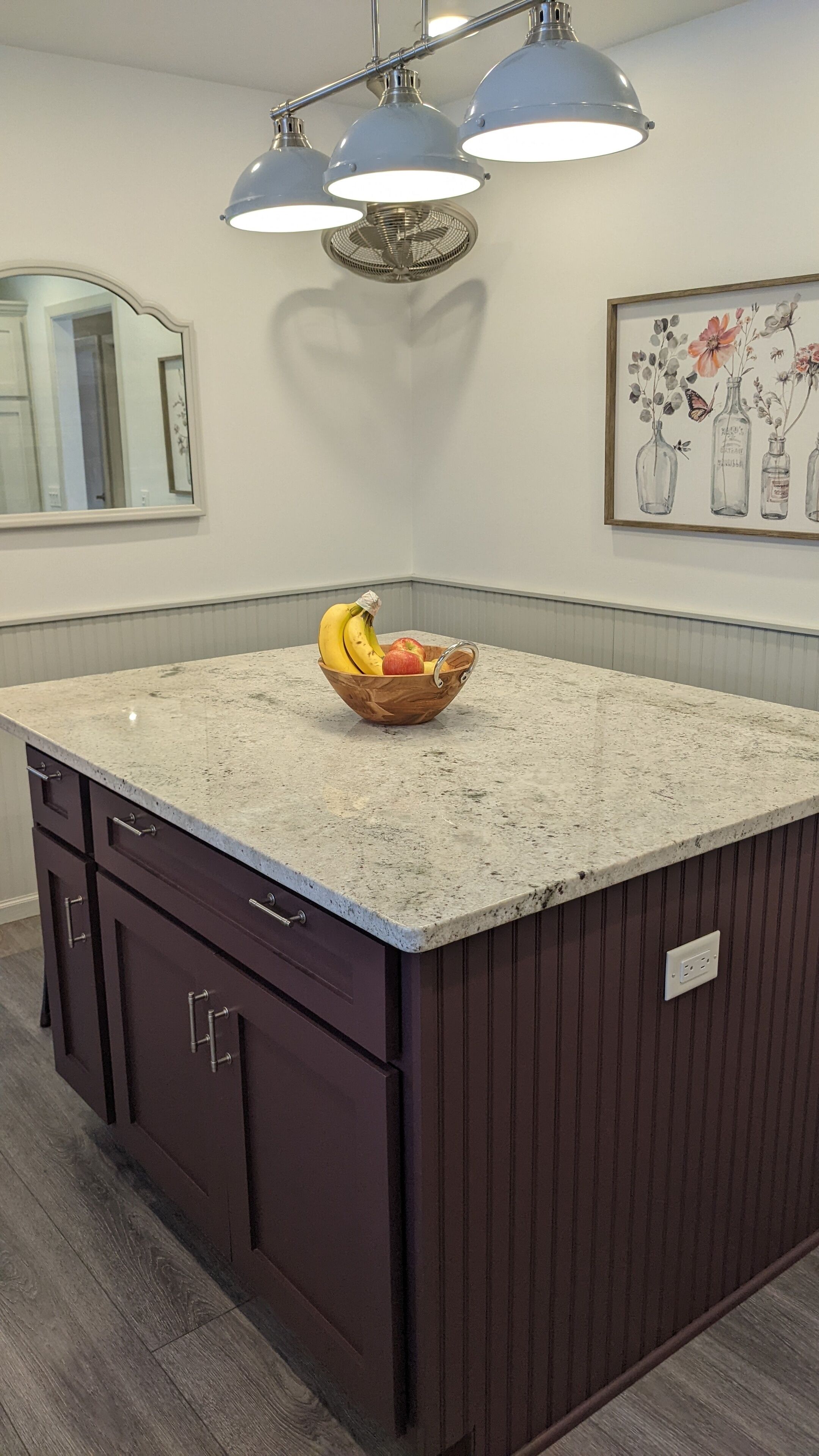A kitchen island with a granite countertop, dark wood cabinets, and a fruit bowl.