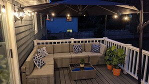A covered outdoor seating area with a sofa and cushions, a small table with a plant, and potted plants. - Elegant Space–Premium Kitchen–Spacious & Ideal for Gathering w/ Friends & Family (Middleton)