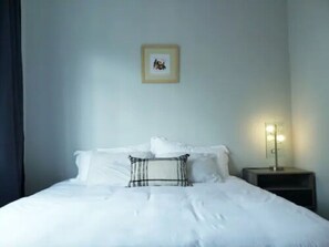 A neatly made bed with white bedding and a black and white pillow. There is a framed picture on the wall above the bed.