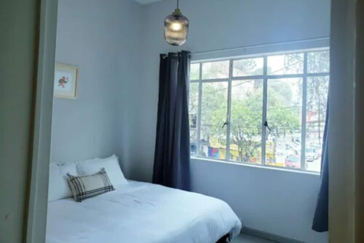 A bedroom with a bed, a window, and a hanging light fixture.