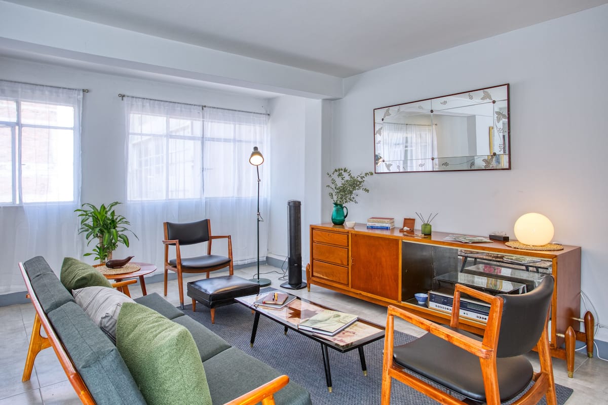 A modern living room with a sofa, chairs, a coffee table, a cabinet, and a large mirror.