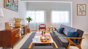 A modern living room with a sofa, a wooden table with breakfast items, a cabinet, and a large window. - Mai Calli Home Rentals (Mexico City)