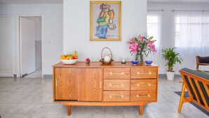 A modern living room with a wooden cabinet, a painting on the wall, a vase with flowers, and a dining area with a chair and table. - Mai Calli Home Rentals (Mexico City)