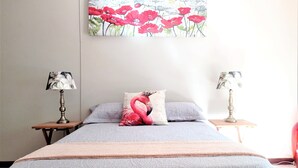 A bedroom with a bed, two nightstands, a lamp on each, and a floral painting above the bed. - Spacious holiday home in cozy complex. Walking distance from the nature reserve. (KZN)