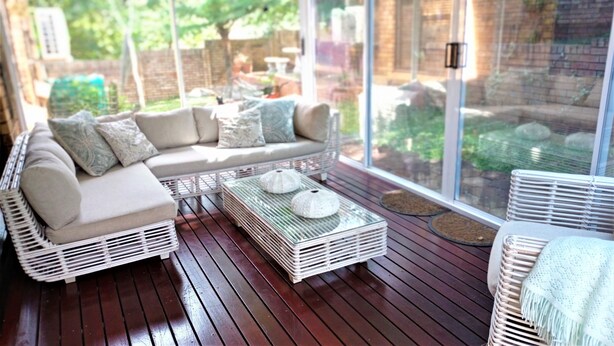 A sunlit patio with a cushioned sofa and wicker chairs, large windows offering a view of the outdoors. - Spacious holiday home in cozy complex. Walking distance from the nature reserve. (KZN)