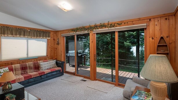 A cozy living room with a sofa, a coffee table, and a lamp. There is a sliding glass door leading to an outdoor deck with a grill. - Fence Lake Retreat w/ dock (Lac du Flambeau)