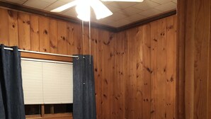 A bedroom with a bed, wooden walls, a ceiling fan, and a window with curtains. - Fence Lake Retreat w/ dock (Lac du Flambeau)