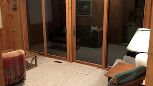 A room with a wooden floor, a wooden chair, a table, and a sliding glass door leading to another room. - Fence Lake Retreat w/ dock (Lac du Flambeau)
