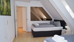 A modern bedroom with a sloped ceiling, a bed with grey bedding, a bedside table with a lamp, and a painting on the wall. - City Center Stays /// AK4-L, duplex apartment (München)