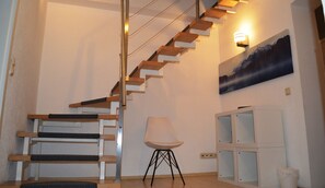 A staircase with wooden steps and a metal railing, a white chair, a cabinet with glass doors, and a wall-mounted light fixture.