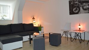 A modern living room with a black sofa, a glass coffee table, a small side table with a lamp, and a chair. - City Center Stays /// AK4-L, duplex apartment (München)