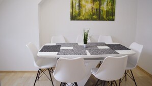 A dining area with a white table, four white chairs, and a painting of a forest on the wall. - City Center Stays /// AK4-L, duplex apartment (München)