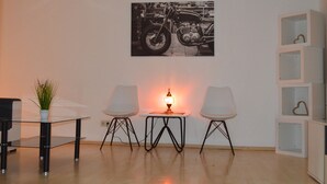 A room with a glass table, two white chairs, a small table with a lamp, and a motorcycle poster on the wall. - City Center Stays /// AK4-L, duplex apartment (München)