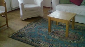 A living room with a white armchair, a wooden coffee table, a white sofa with colorful cushions, a bookshelf, and a large window with natural light. - No 2 Old Town Apts is in the centre of Bohinjska Bistrica, close to amenities. (Radovljica)