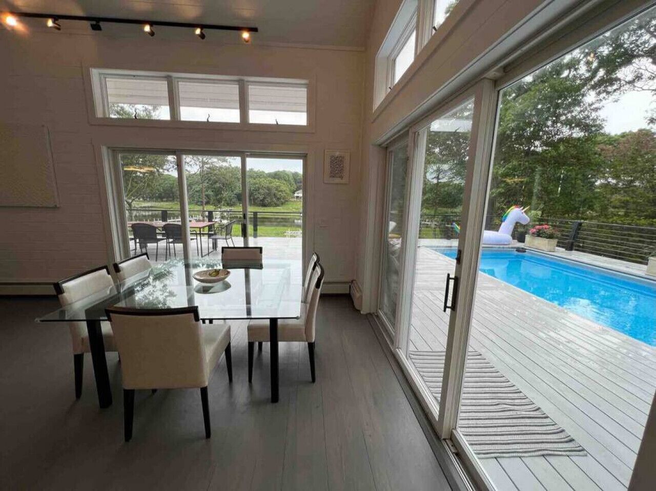 A spacious room with a glass table and chairs, large windows, and a view of a swimming pool.
