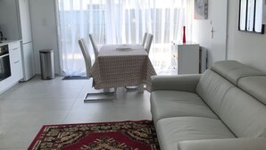 A modern living room with a sofa, a dining table with chairs, a chandelier, and a large window with sheer curtains. - Studio 35m² with large garden, train station 5 min, parking, wifi THD, near beach (Vannes)