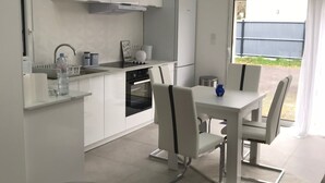 A modern kitchen with white cabinets, a built-in oven, and a dining area with a glass table and chairs. - Studio 35m² with large garden, train station 5 min, parking, wifi THD, near beach (Vannes)