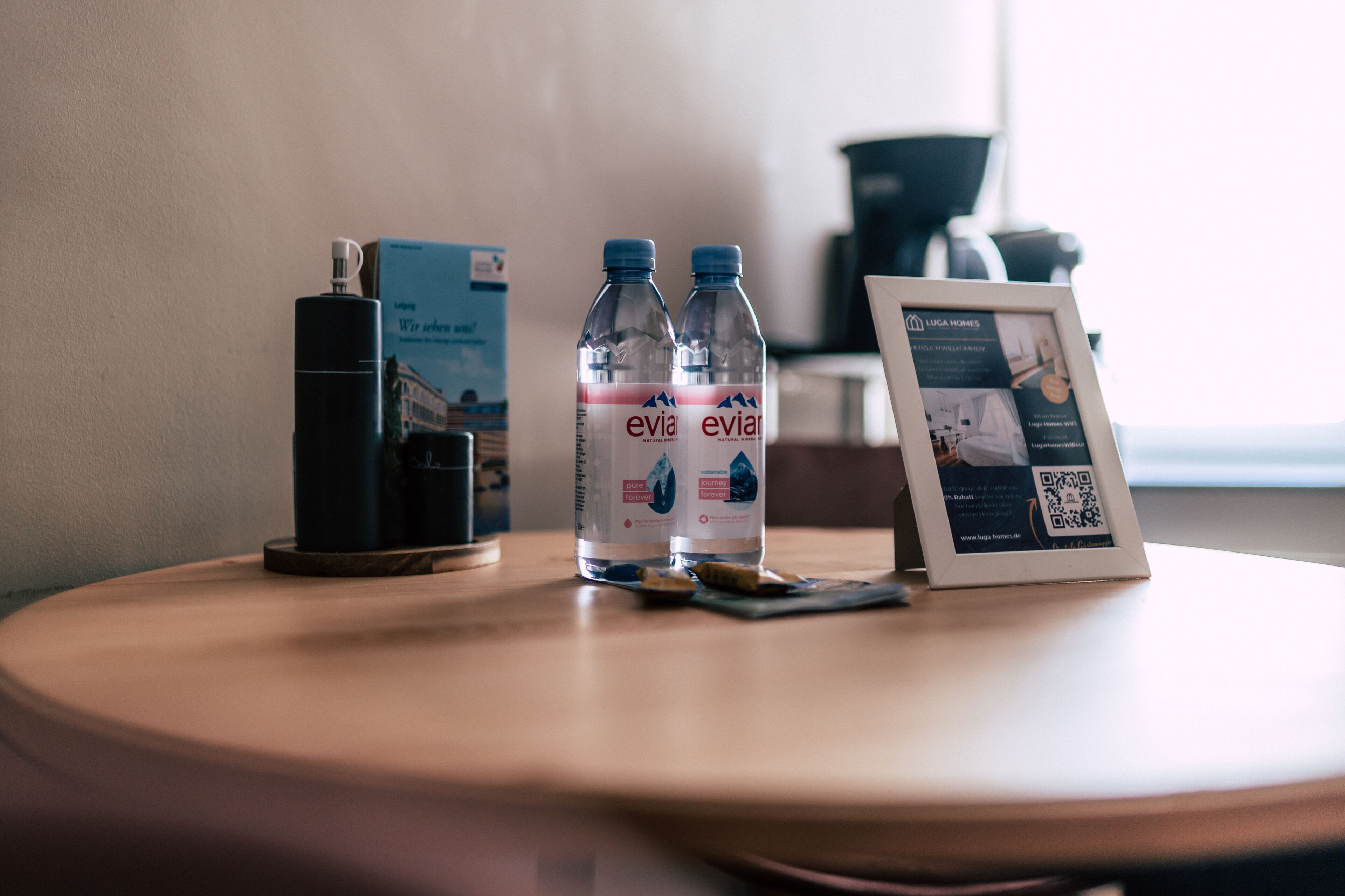 Una mesa con dos botellas de Evian, un folleto de LUGA HOMES y una foto enmarcada sobre una mesa de madera.