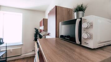 A microwave on a wooden countertop in a kitchen with a window and cabinets in the background.