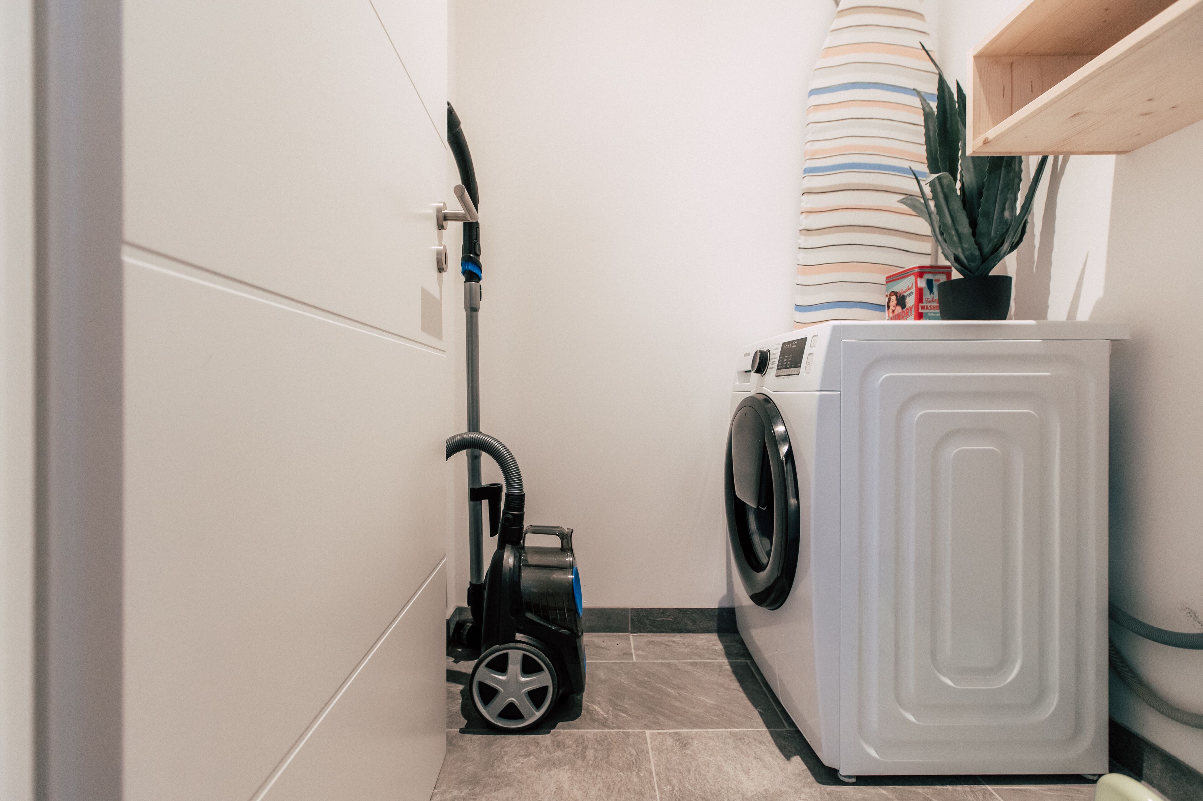 A laundry room with a washing machine and a vacuum cleaner.