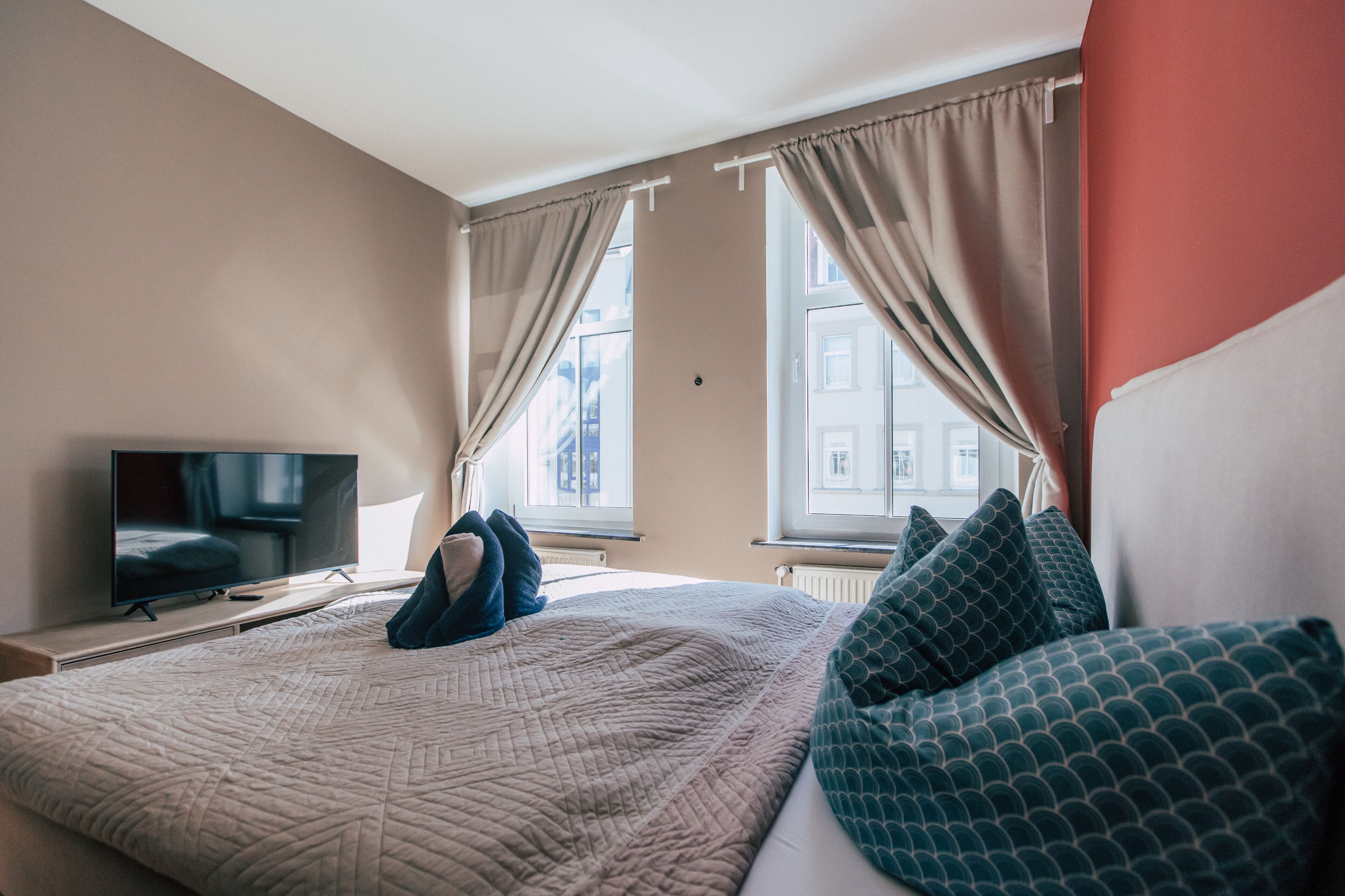 A hotel room with a bed, a TV, and a window with curtains.