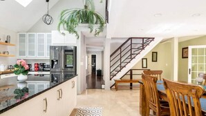A modern kitchen with a central island, a dining area with wooden chairs, a staircase, and a hallway leading to another room. - Luxury Private Estate Mins to Winery /Brewery (Leesburg)