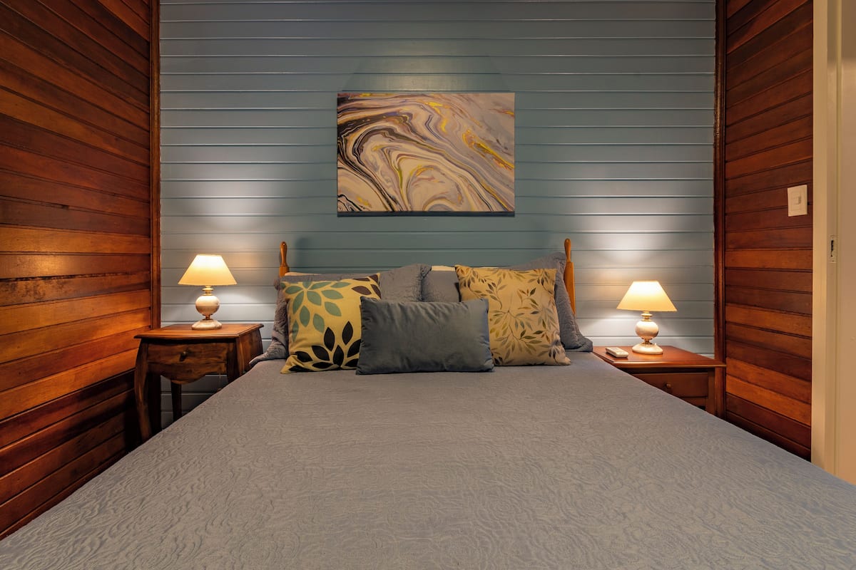 Une chambre à coucher avec un lit, deux tables de chevet avec des lampes et un grand tableau abstrait accroché au mur.