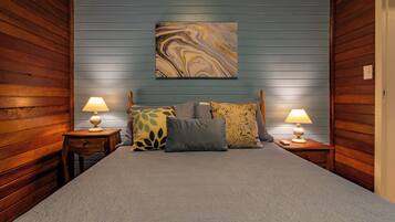 Un dormitorio con una cama, dos mesitas de noche con lámparas y un cuadro abstracto grande en la pared.