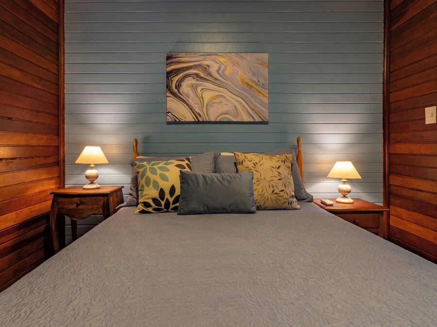 Un dormitorio con una cama, dos mesitas de noche con lámparas y un cuadro abstracto grande en la pared.