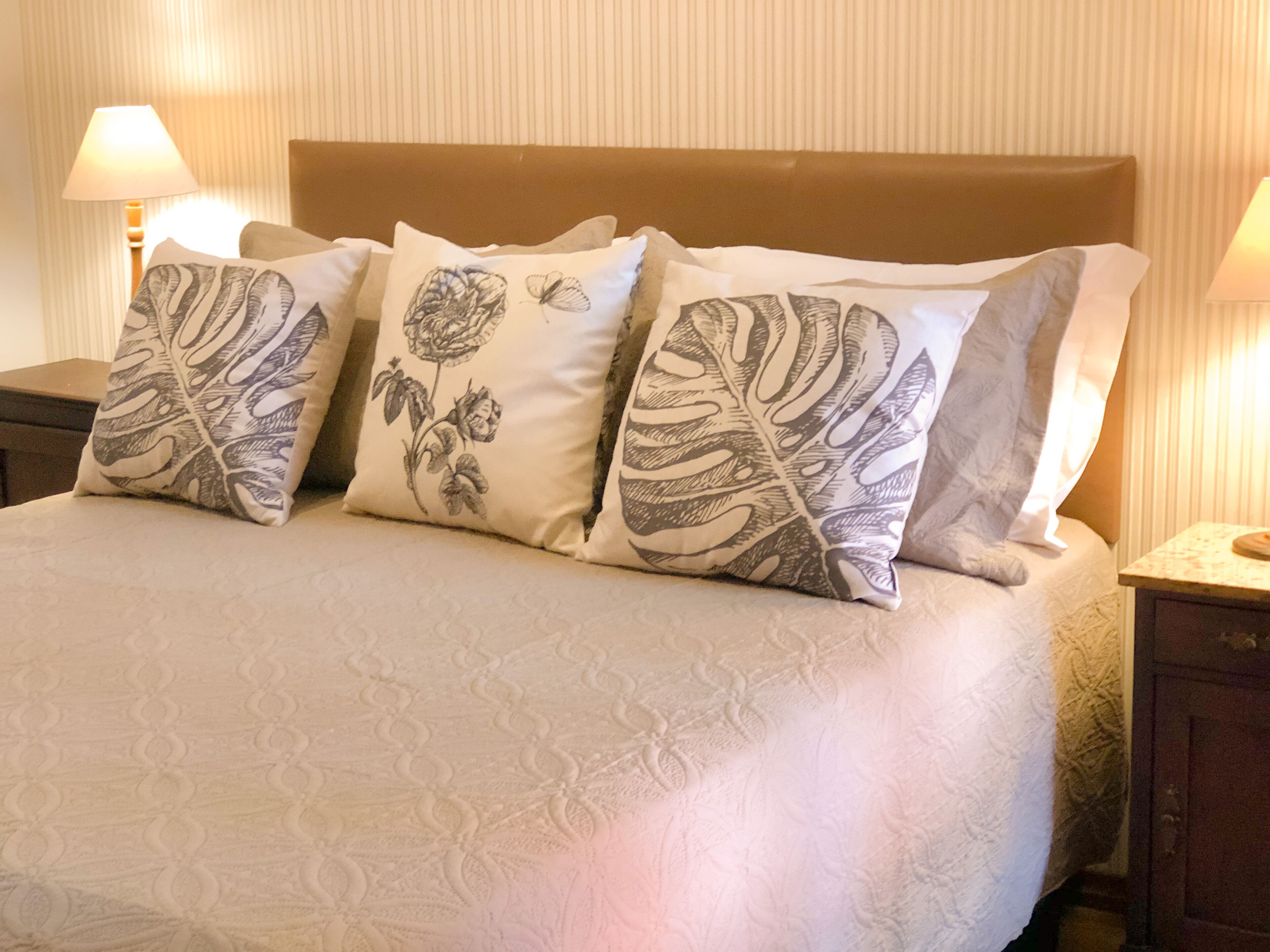 Una cama con colcha estampada y tres almohadones decorativos con diseños de hojas y flores.