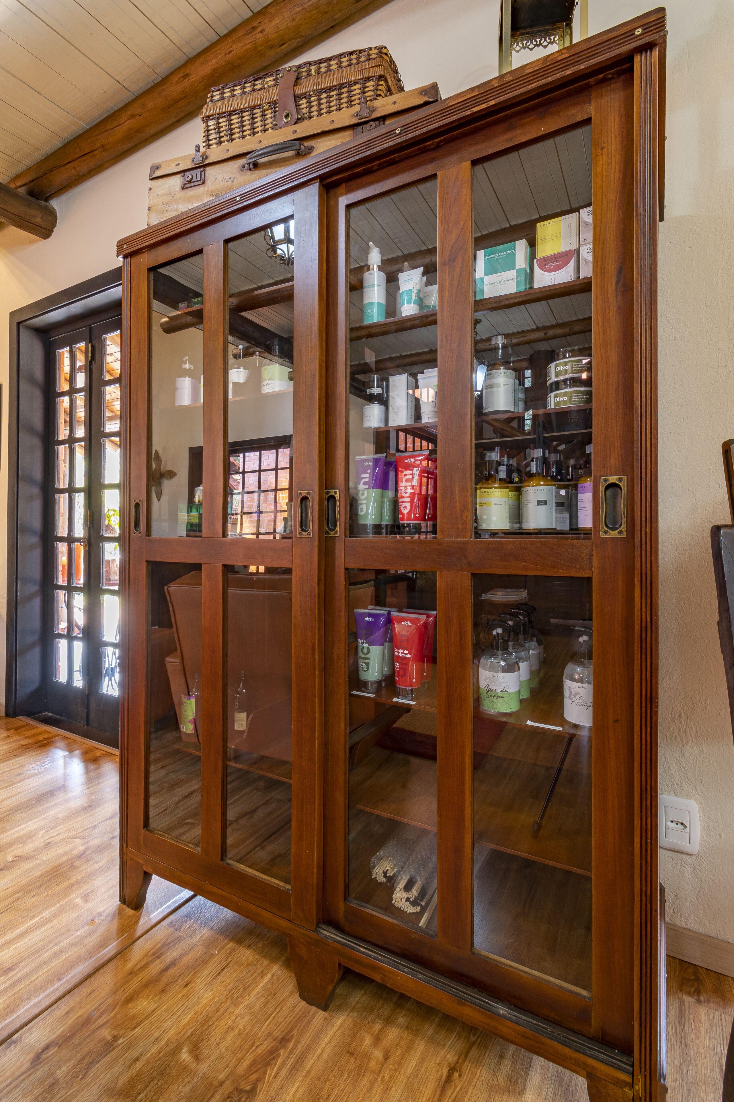 A wooden cabinet with glass doors containing various toiletries and personal care products.