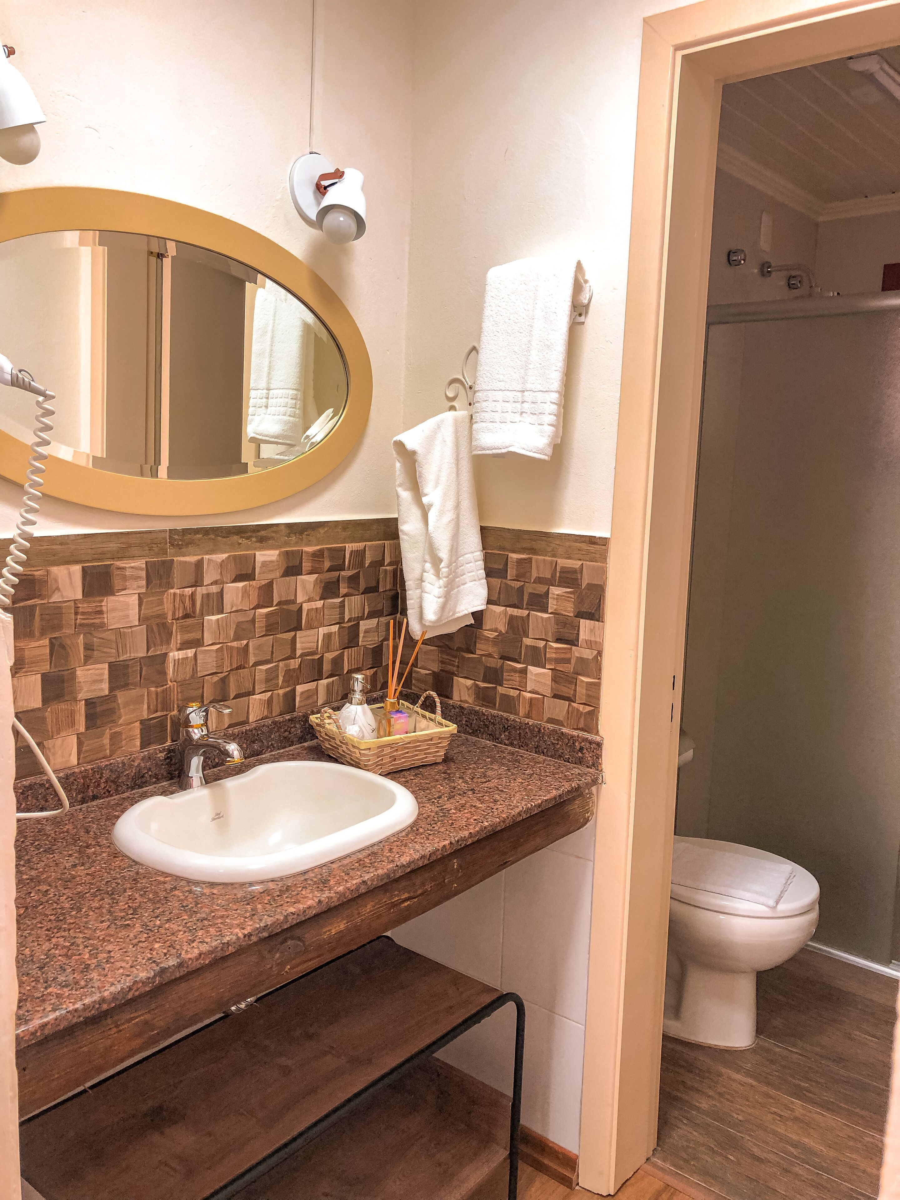 A bathroom with a granite countertop, a white sink, a mirror, a towel rack, and a toilet.