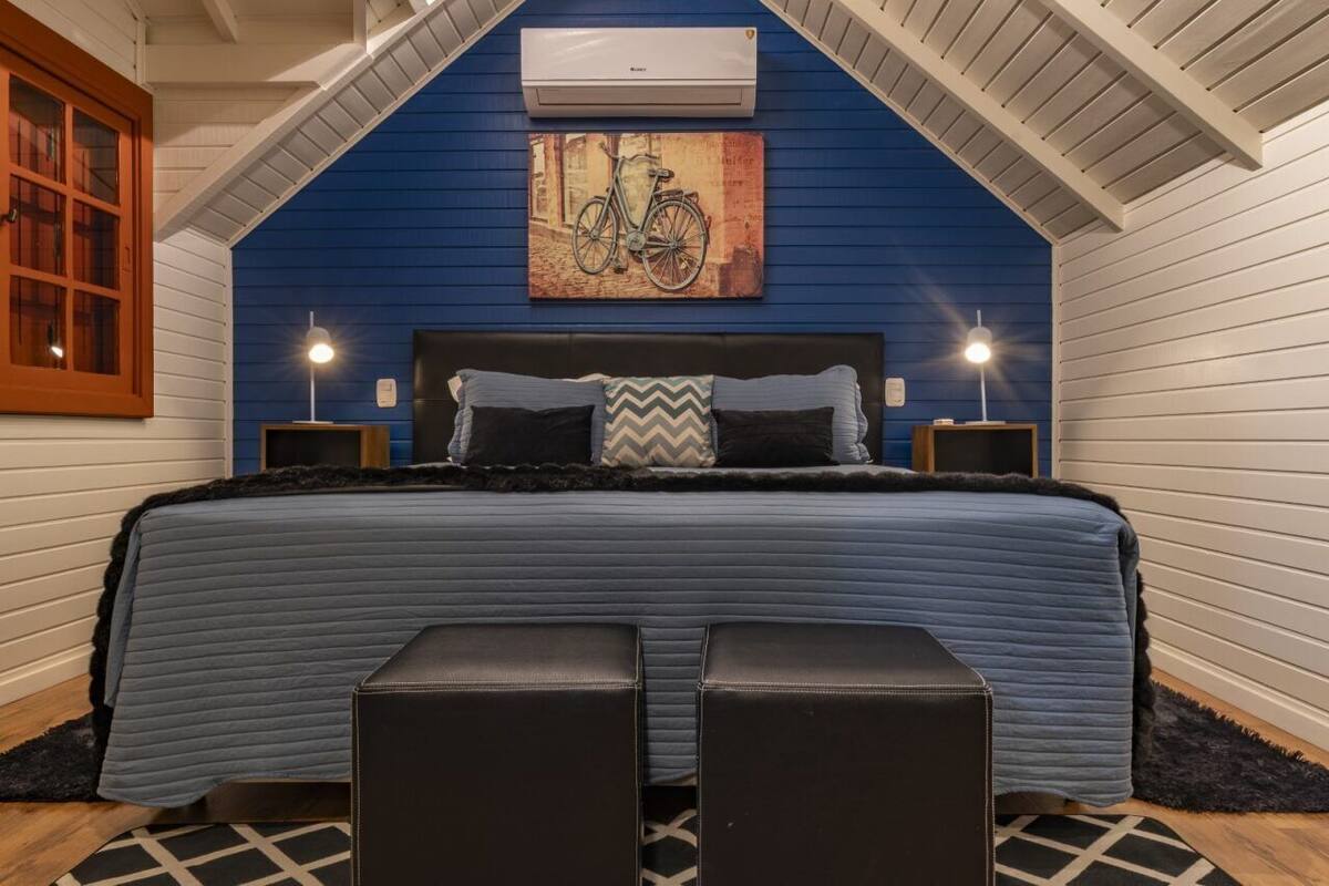 Une chambre avec un mur bleu, un lit avec une tête de lit noire, deux tables de chevet et un tableau représentant un vélo accroché au mur.