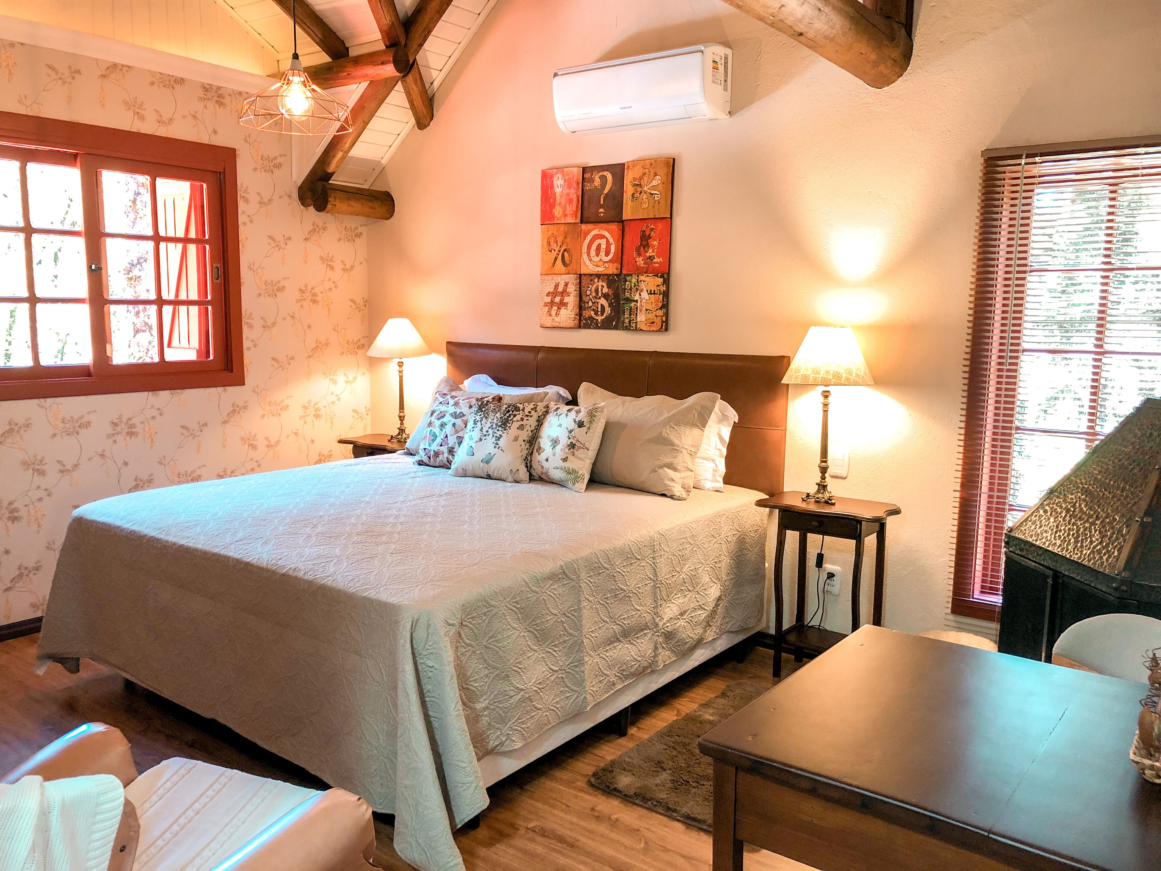 Une chambre à coucher avec un grand lit, deux tables de chevet avec des lampes, une tête de lit en bois, un papier peint à motifs floraux et une fenêtre avec des stores.