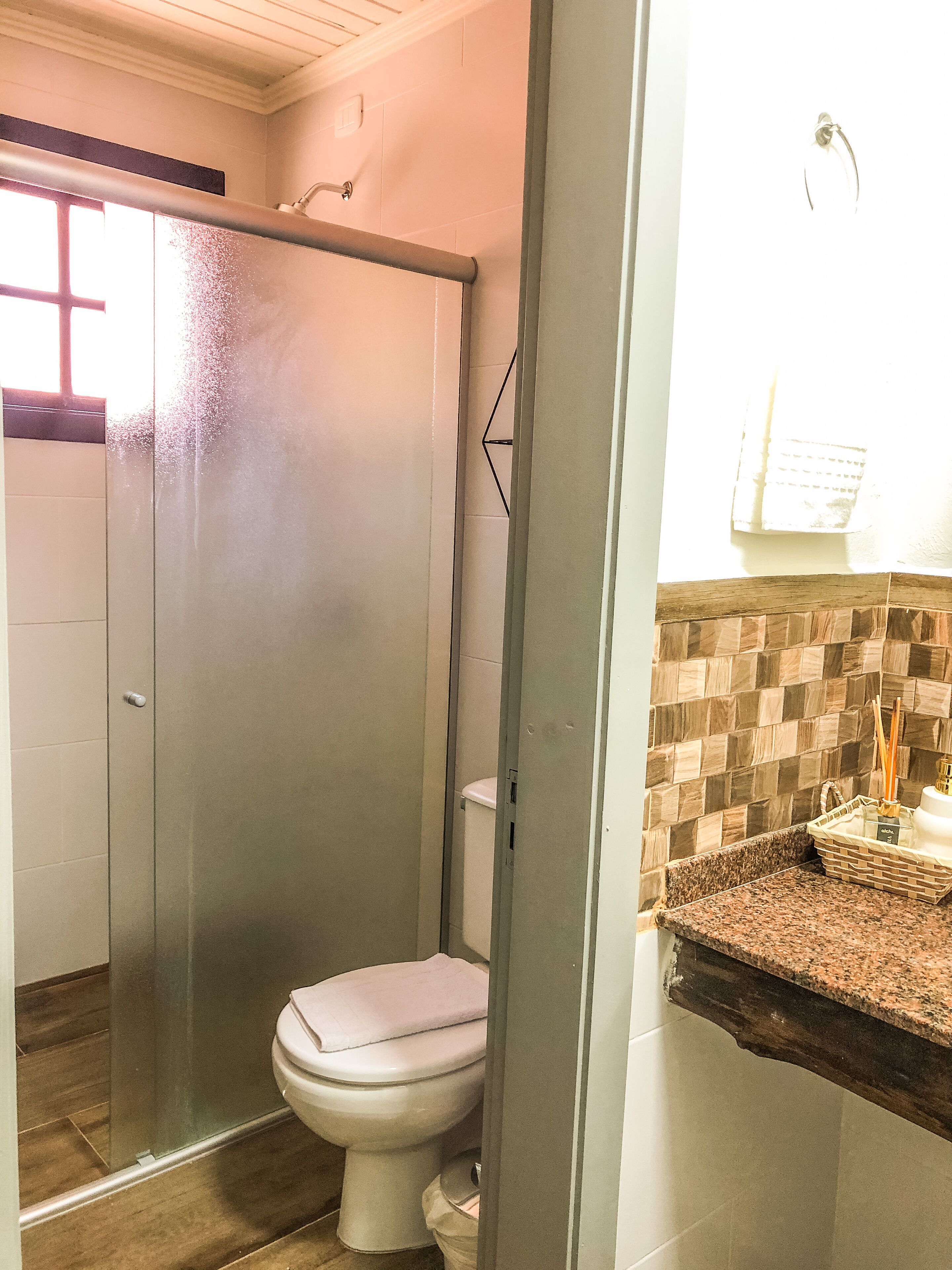 Une salle de bain comprenant des toilettes, une douche et un coin lavabo avec un porte-serviettes et un panier.