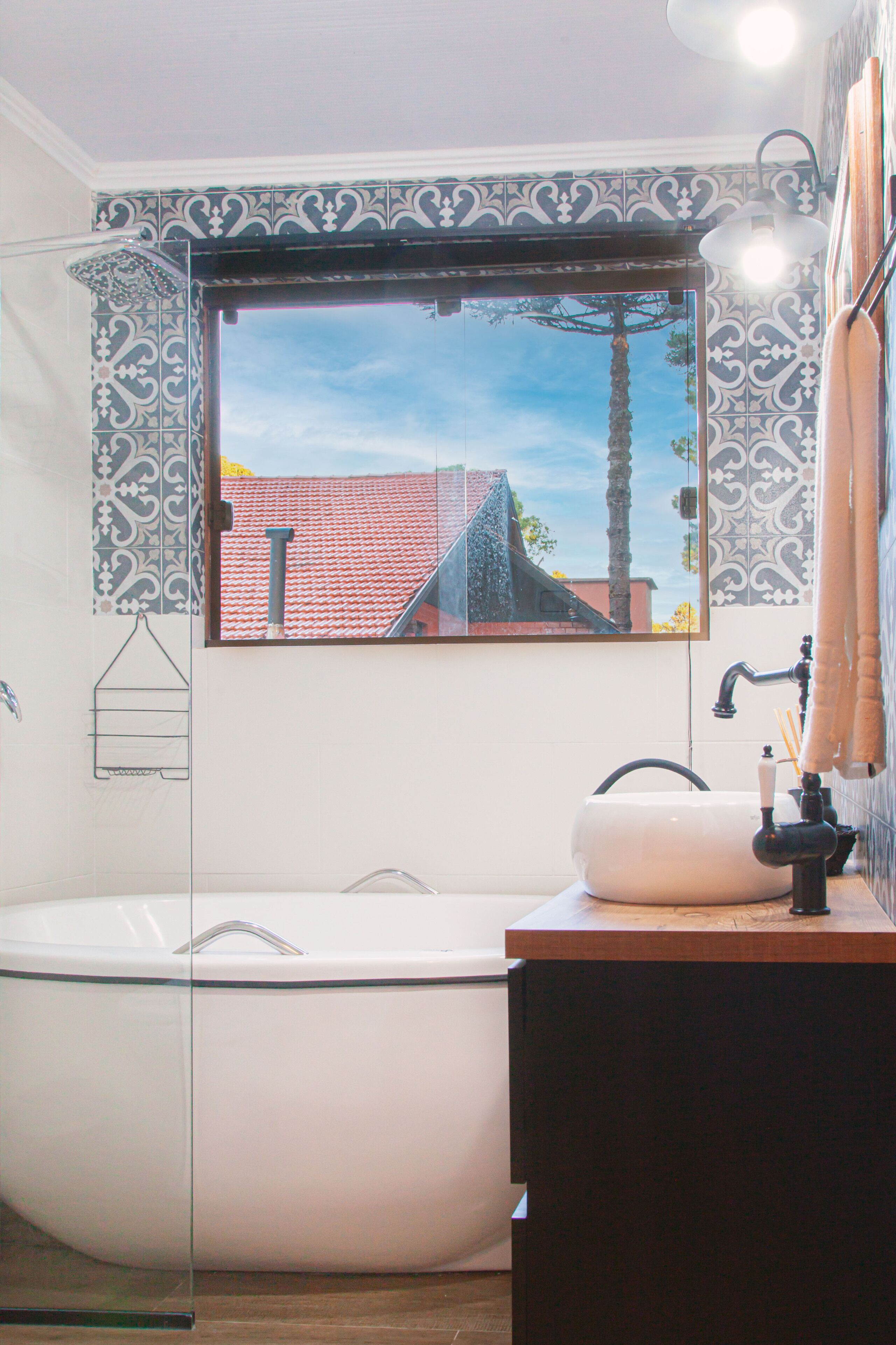 Un baño con una bañera independiente, un lavamanos con espejo y una ventana con vistas a edificios y una palmera.