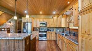 Une cuisine spacieuse dotée de meubles en bois, de plans de travail en granit, d’appareils électroménagers en acier inoxydable et de luminaires suspendus.